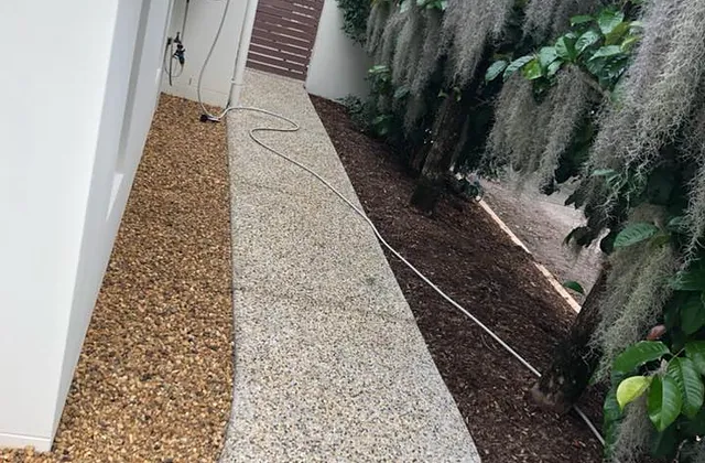 Light exposed aggregate path running down the side of a house beside a garden bed