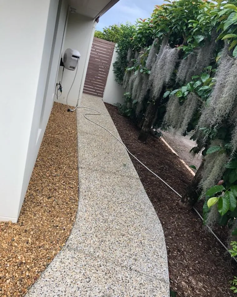 Light exposed aggregate path running down the side of a rendered house beside a garden bed