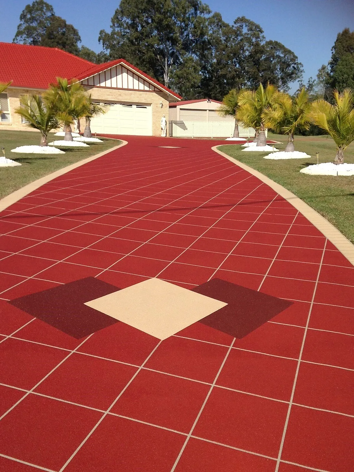 Coloured and stencilled concrete driveway curving to a double garage, bordered by palms